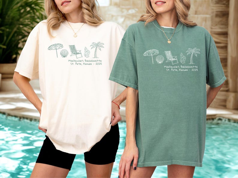 May include: Two oversized t-shirts, one cream and one sage green, featuring a beach-themed graphic and text. The graphic includes an umbrella, seashell, chair, and palm tree. The text reads "Mackenzie's Bachelorette St. Pete, Florida - 2025."