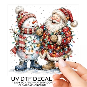 May include: A UV DTF decal featuring a snowman wearing a red and white striped hat and scarf with blue boots, standing next to a laughing Santa Claus in a red suit and brown boots, both wrapped in colorful Christmas lights on a clear background.
