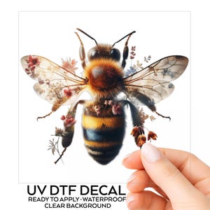 May include: A UV DTF decal featuring a detailed bee with yellow and black stripes, fuzzy brown thorax, and translucent wings decorated with small floral patterns. The text below reads UV DTF DECAL READY TO APPLY WATERPROOF CLEAR BACKGROUND.