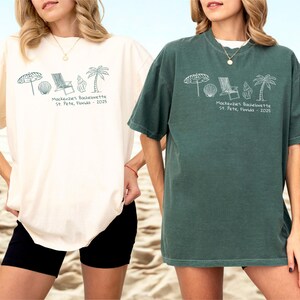 May include: Two women wearing oversized t-shirts. One is cream-colored, the other is dark green. Both shirts feature a beach-themed graphic and the text "Mackenzie's Bachelorette St. Pete, Florida - 2025". The shirts are paired with black shorts.
