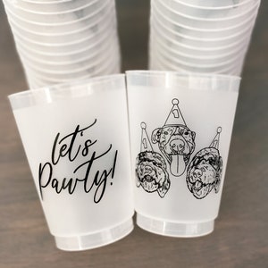 May include: Frosted plastic cups with black text and dog illustrations. One cup says "let's Pawty!" in script. The other cup features three dogs wearing party hats. A stack of cups is visible in the background.