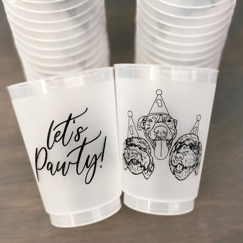 May include: Frosted plastic cups with black text and dog illustrations. One cup says "let's Pawty!" in script. The other cup features three dogs wearing party hats. A stack of cups is visible in the background.