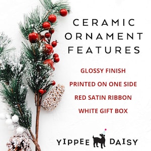 K&ouml;nnte beinhalten: Keramik-Weihnachtsbaumschmuck mit gl&auml;nzender Oberfl&auml;che. Der Schmuck ist einseitig bedruckt und hat ein rotes Satinband. Er wird in einer wei&szlig;en Geschenkbox geliefert. Der Schmuck ist mit einem festlichen gr&uuml;nen Tannenzweig mit roten Beeren und einer Tannenzapfen verziert.