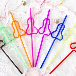 May include: A set of eight colourful plastic straws with a unique bend in the shape of a heart. The straws are arranged in a fan shape on a white lace background.