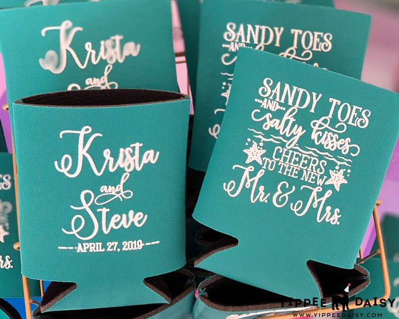 May include: Teal blue can coolers with white text. One cooler says "Sandy Toes and Salty Kisses Cheers to the New Mr. & Mrs." The other cooler says "Krista and Steve - April 27, 2019 - "