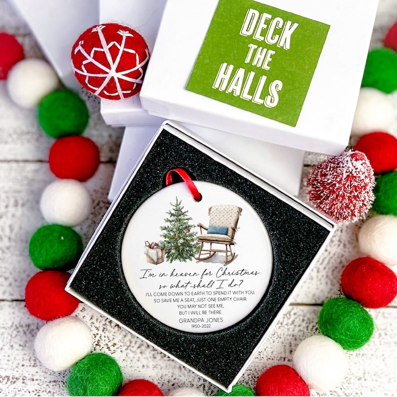 May include: A white ceramic Christmas bauble featuring a watercolour illustration of a rocking chair and a Christmas tree. The ornament includes the text "I'm in heaven for Christmas so what shall I do? I'll come down to earth to spend it with you so save me a seat, just one empty chair. You may not see me, but I will be there. Grandpa Jones 1950-2022".