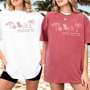 May include: Two oversized t-shirts, one white and one red, featuring a beach-themed graphic in red ink. The design includes an umbrella, seashell, beach chair, ice cream cone, and palm tree. Text reads "Mackenzie's Bachelorette St. Pete, Florida - 2025".