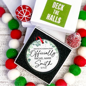 Op de afbeelding: Een witte keramische kerstbal met een groen eucalyptusbladerenontwerp. De kerstbal zegt "Officially" met de naam "Rachel Marie Smith" en de datum "12.17.22".