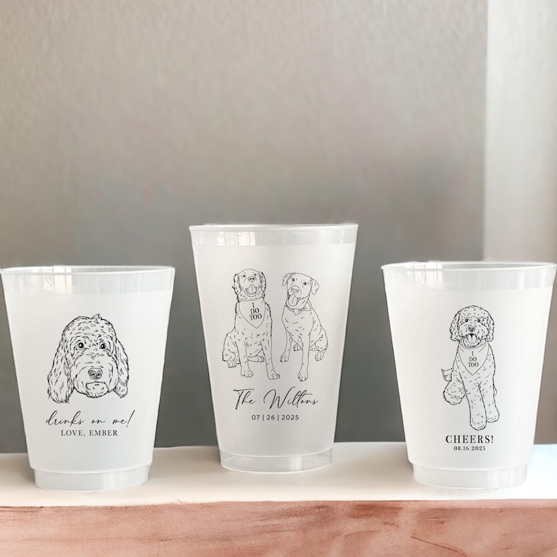 May include: Three clear plastic cups with black line drawings of dogs. One cup has the text "Drinks on me! Love, Ember". The center cup has two dogs and the text "The Willtons 07|26|2025". The third cup has a dog and the text "Cheers! 08.16.2025".
