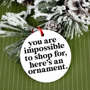 K&ouml;nnte beinhalten: Wei&szlig;er Keramik-Weihnachtsbaumschmuck mit schwarzem Text, der "Du bist unm&ouml;glich zu beschenken, hier ist ein Ornament." lautet.