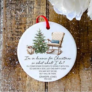 May include: White ceramic Christmas bauble featuring a hand-painted image of a rocking chair, a Christmas tree, and a basket of gifts. The ornament includes the text "I'm in heaven for Christmas so what shall I do? I'll come down to earth to spend it with you. So save me a seat, just one empty chair. You may not see me, but I will be there. Grandpa Jones 1950-2022".