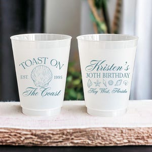 K&ouml;nnte beinhalten: Zwei wei&szlig;e Plastikbecher mit blauem Text und Grafiken. Der linke Becher sagt "Toast On Est. 1995 The Coast" mit einer Muschelgrafik. Der rechte Becher sagt "Kristen's 30th Birthday Key West, Florida" mit Muschel- und Seestern-Grafiken.