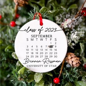 May include: White ceramic bauble with a black calendar for September 2023, featuring the text "class of 2023" and "Brennen Rossman" with the University of Utah logo.