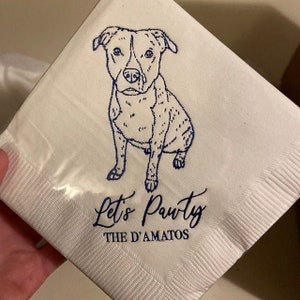 May include: White paper napkin with a blue line drawing of a dog sitting. The text "Let's Pawty" and "The D'Amatos" is printed in blue below the dog.