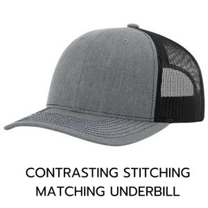 May include: A gray and black trucker hat with a contrasting navy blue stitching detail. The hat has a mesh back and a solid front panel.