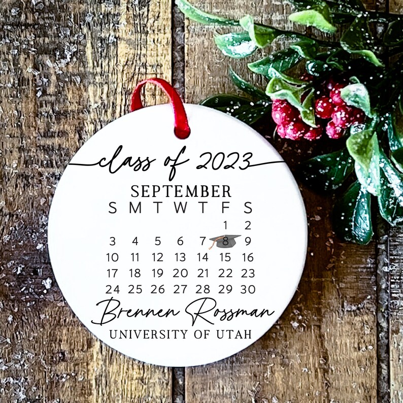 May include: White round bauble with a black calendar for September 2023, the text "class of 2023", a graduation cap icon, and the name "Brennen Rossman" with the text "UNIVERSITY OF UTAH" underneath.