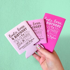 May include: Three pink and light pink can coolers with the text "Boots, Booze & Birthday" and a cowboy-themed graphic. The coolers also feature the text "Emme's 21st Rodeo, Nashville, TN".