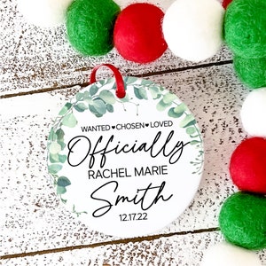 Op de afbeelding: Ronde witte ornament met groene eucalyptusbladeren en de tekst "WANTED &hearts; CHOSEN &hearts; LOVED Officially Rachel Marie Smith 12.17.22"