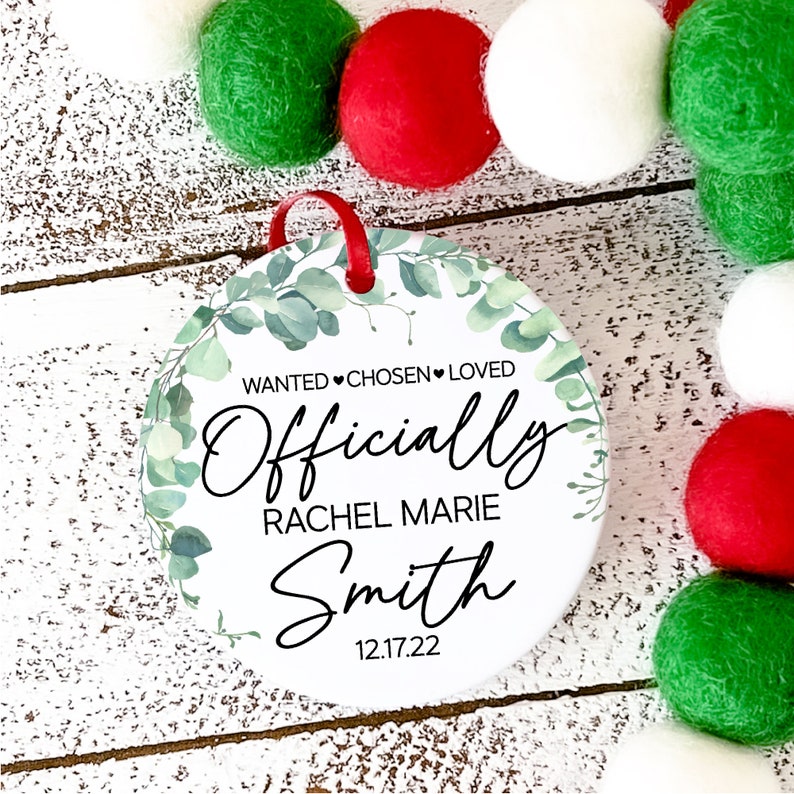 Op de afbeelding: Ronde witte ornament met groene eucalyptusbladeren en de tekst "WANTED &hearts; CHOSEN &hearts; LOVED Officially Rachel Marie Smith 12.17.22"