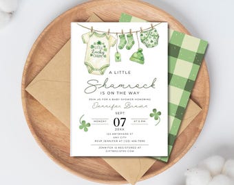 May include: A baby shower invitation with a shamrock theme. The invitation features a watercolor illustration of baby clothes hanging on a clothesline. The text reads "A Little Shamrock is on the Way."