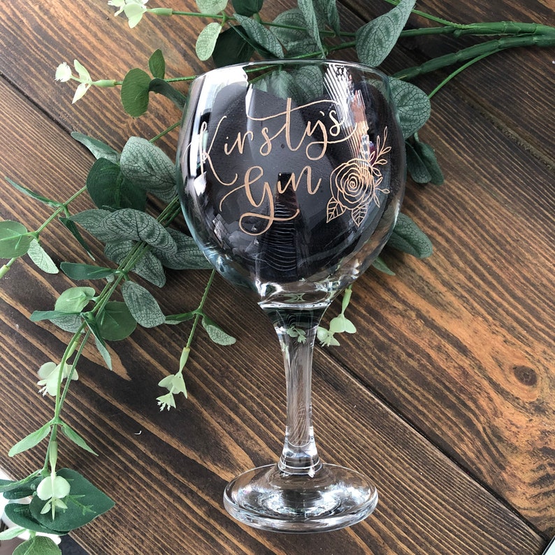 May include: A clear glass gin glass with a gold design that says "Kirsty's Gin" with a rose and leaves.