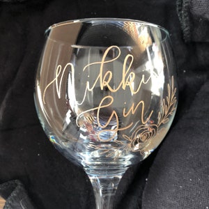 May include: A clear glass gin glass with gold lettering that says "Nikki Gin" and a gold floral design.