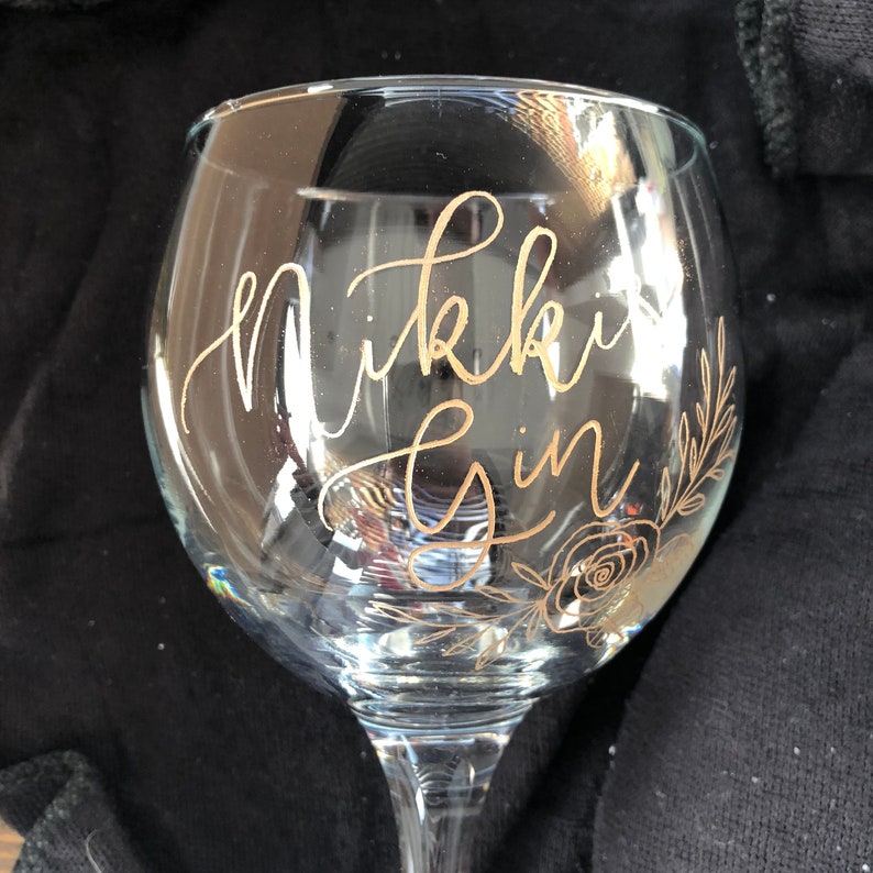 May include: A clear glass gin glass with gold lettering that says "Nikki Gin" and a gold floral design.