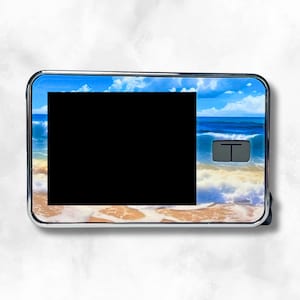 May include: A silver and black digital device with a blue, white, and brown beach scene design. The device has a black screen and a small button on the right side.