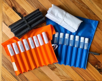 May include: Two fabric pouches with clear tubes labeled with different names. The pouches are orange and blue and are rolled up. The pouches are on a wooden surface.