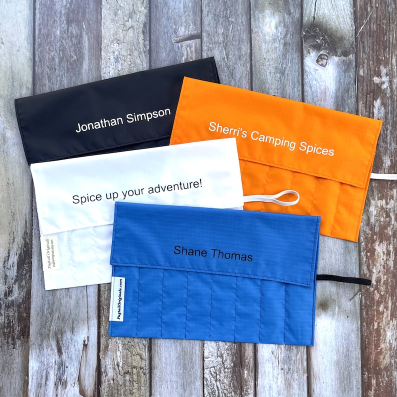 Puede incluir: Cuatro bolsas enrollables para especias personalizadas en negro, blanco, naranja y azul. Las bolsas est&aacute;n hechas de tela y tienen un cierre de cremallera. Las bolsas est&aacute;n etiquetadas con los nombres "Jonathan Simpson", "Sherri's Camping Spices", "Spice up your adventure!" y "Shane Thomas".