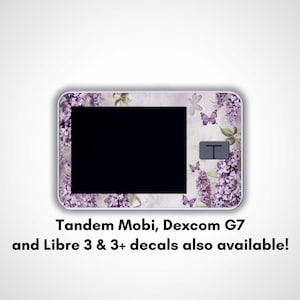 May include: A rectangular device with a black screen, adorned with a floral and butterfly design in shades of purple and green. The text at the bottom reads "Tandem Mobi, Dexcom G7 and Libre 3 & 3+ decals also available!"