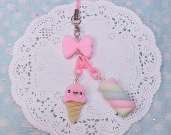 Puede incluir: Un amuleto rosa y blanco con un lazo rosa, un cono de helado rosa con una carita sonriente y un malvavisco en espiral pastel. Los amuletos están unidos a una cadena rosa y plateada.