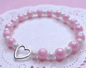 Könnte beinhalten: Ein rosa-weißes Perlenarmband mit einem silbernen Herz-Anhänger.