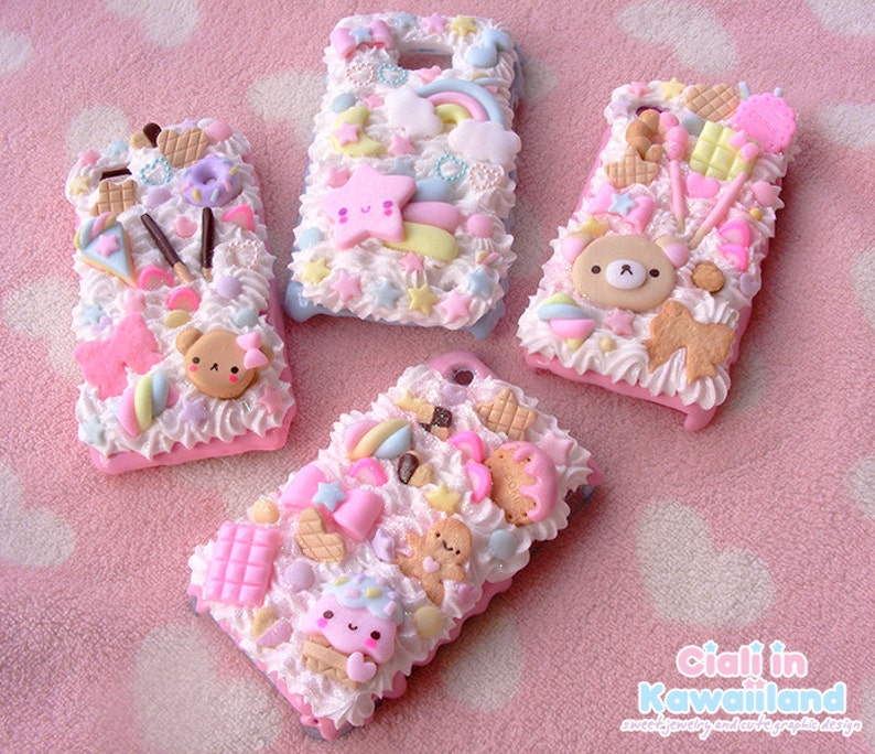 May include: Four pink and white decorated phone cases with various kawaii designs, including a rainbow, stars, a bear, and a gingerbread man. The cases are covered in white frosting and decorated with sprinkles, candies, and other cute details.