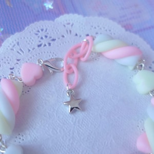 Pode incluir: Um bracelete de amuletos de marshmallow rosa, branco e amarelo com um amuleto de estrela prateada e um fecho prateado.