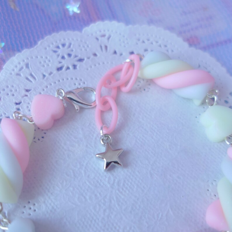 Pode incluir: Um bracelete de amuletos de marshmallow rosa, branco e amarelo com um amuleto de estrela prateada e um fecho prateado.