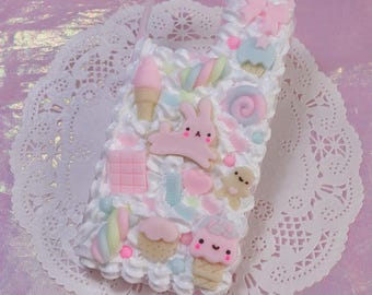 May include: A phone case decorated with white whipped cream texture and various pastel-coloured charms including a pink rabbit, ice cream cones, a cupcake, a swirl lollipop, a gingerbread man, a chocolate bar, and a bow in shades of pink, blue, and yellow.