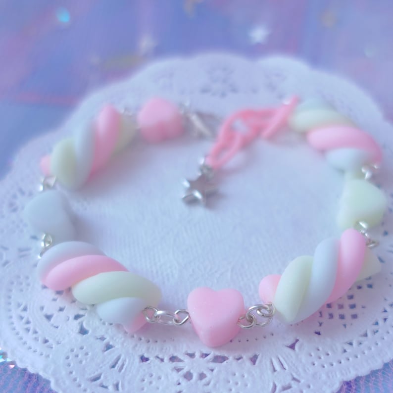Pode incluir: Um bracelete de charme de marshmallow rosa pastel, branco e amarelo com um charme de estrela prateada. O bracelete &eacute; feito de uma corrente prateada e tem um charme em forma de cora&ccedil;&atilde;o.