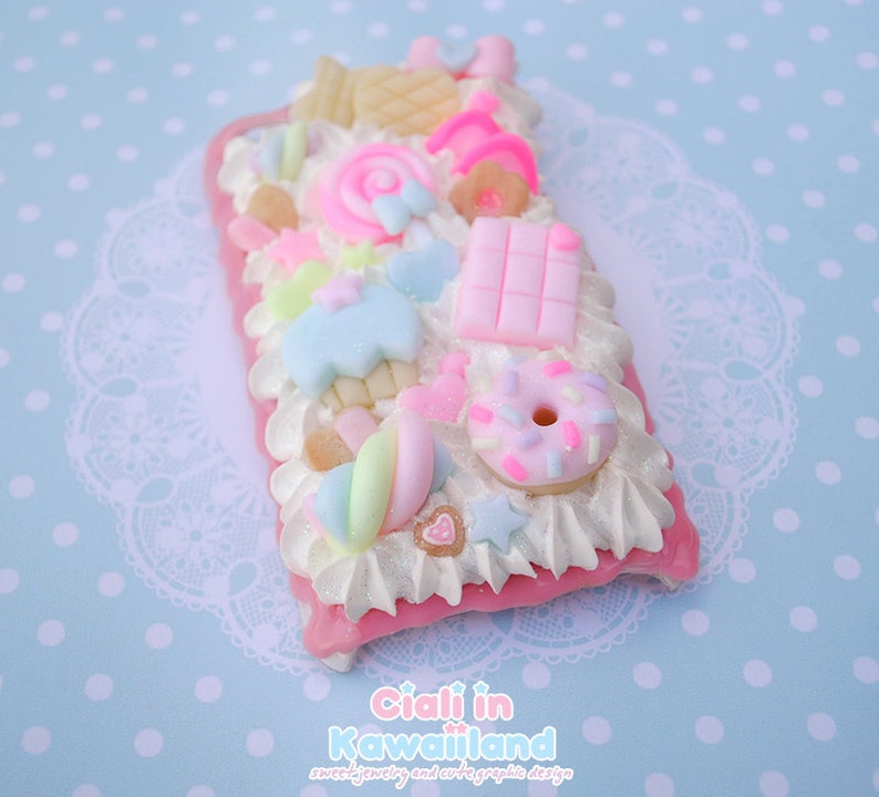 May include: A pink and white phone case decorated with colourful candy and sweets, including a doughnut, a lollipop, and marshmallows. The case is covered in glitter and has a white background.