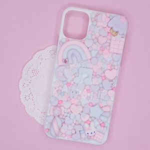 May include: A white phone case decorated with a pink, blue and white pastel rainbow, hearts, stars and music notes. The case is covered in small, colourful sprinkles.