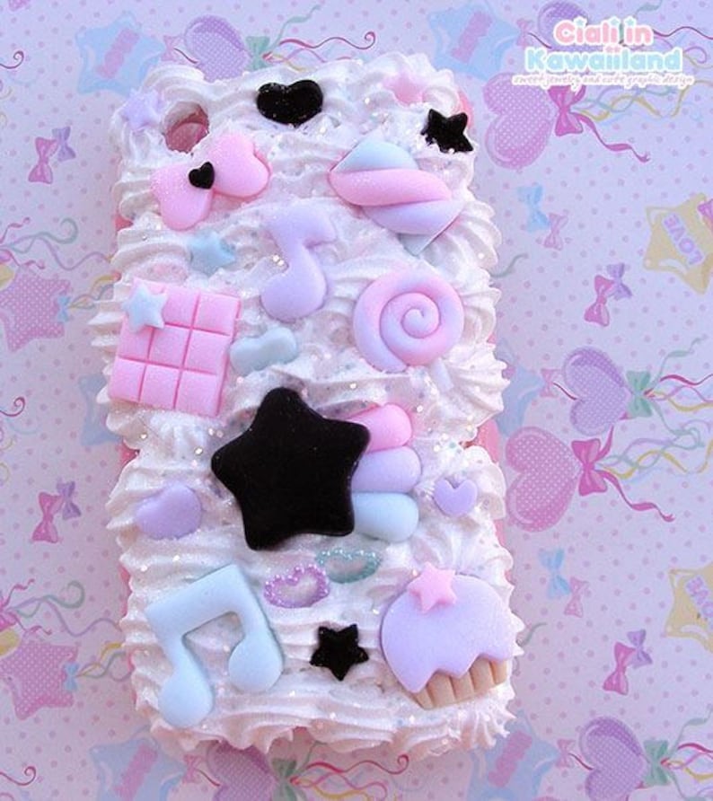 May include: A white phone case decorated with pastel pink, blue, and white 3D candy and star shapes. The case is covered in white frosting and has a glittery finish.