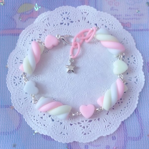 Pode incluir: Um bracelete com pingentes de marshmallow rosa, branco e amarelo com um pingente de estrela prateada e pingentes de cora&ccedil;&atilde;o.