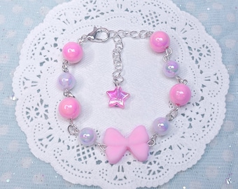 May include: A pink and iridescent beaded bracelet with a silver chain and a pink bow charm. The bracelet also has a silver star charm.