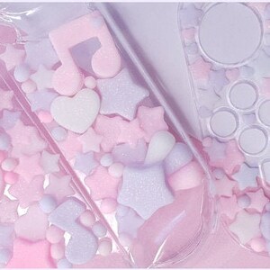Puede incluir: Una funda de pl&aacute;stico transparente con un dise&ntilde;o rosa y morado. La funda est&aacute; llena de peque&ntilde;as formas de colores pastel, incluyendo estrellas, corazones y notas musicales. La funda est&aacute; dise&ntilde;ada para contener una Nintendo Switch.