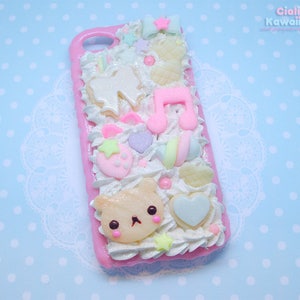 May include: A pink phone case decorated with white frosting, colourful sprinkles, and various 3D embellishments, including a bear, a star, a music note, and a heart. The text "Ciali in Kawaiiland" is printed in the top right corner.