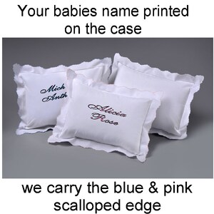 Peut inclure: Trois oreillers blancs pour bébé avec des bords festonnés. Chaque oreiller porte un nom brodé en écriture cursive. Le texte en haut dit "Your babies name printed on the case" et le texte en bas dit "we carry the blue & pink scalloped edge."