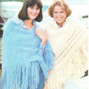 May include: Two women wearing knitted shawls with fringe. The shawl on the left is light blue and the shawl on the right is cream.