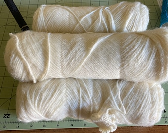 May include: Three skeins of white yarn, stacked on top of each other. The yarn is soft and fluffy, and it is perfect for knitting or crocheting.