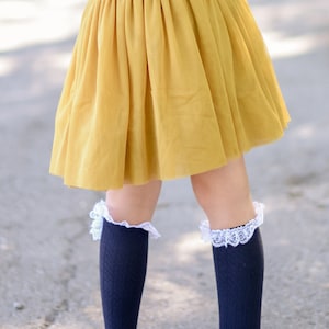 May include: A young person wearing a yellow tulle skirt with a purple top and black knee-high socks with white lace trim. They are wearing leopard print flats.