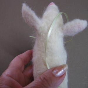 May include: A white felt animal with a pink nose and light green ribbon tied around its body.